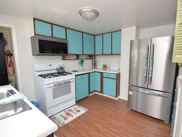 kitchen featuring baseboards, light wood-type flooring, light countertops, stainless steel appliances, and blue cabinetry