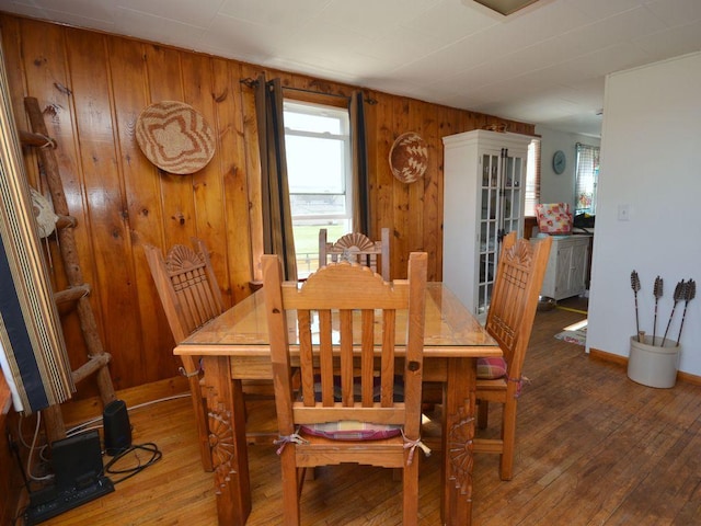 dining room featuring baseboards, wood walls, and hardwood / wood-style flooring