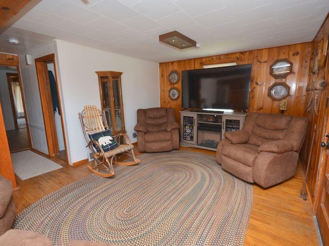 living area featuring light wood-style floors, baseboards, and wood walls