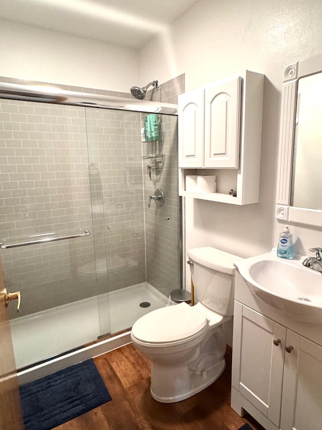 bathroom featuring vanity, toilet, wood finished floors, and a stall shower