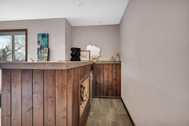 bar featuring wooden walls, baseboards, and a bar