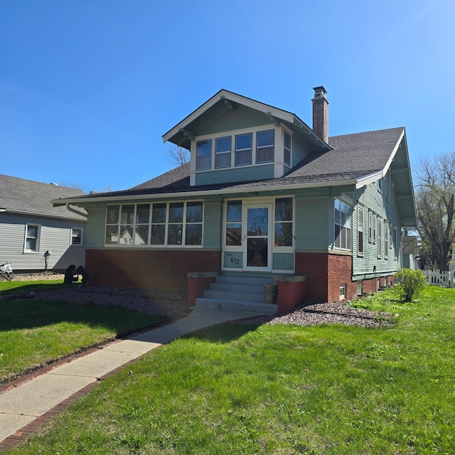 bungalow-style home featuring a chimney, brick siding, a front yard, a shingled roof, and entry steps