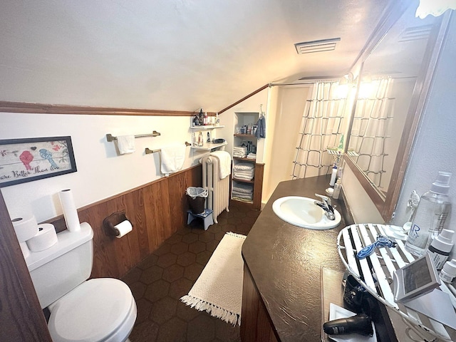 bathroom featuring toilet, wooden walls, lofted ceiling, a wainscoted wall, and vanity