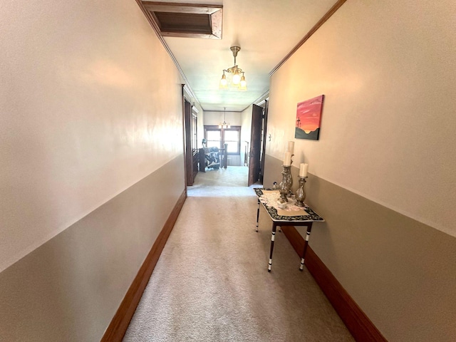 hallway with baseboards, a chandelier, carpet, and ornamental molding