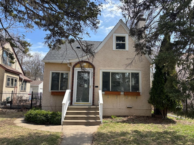 view of front facade featuring fence, a chimney, roof with shingles, and stucco siding
