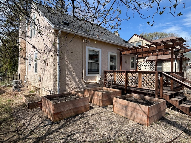 rear view of house featuring a wooden deck, a pergola, fence, stucco siding, and a vegetable garden