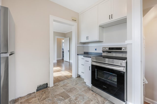 kitchen featuring appliances with stainless steel finishes, white cabinetry, dark countertops, baseboards, and light stone finish floors