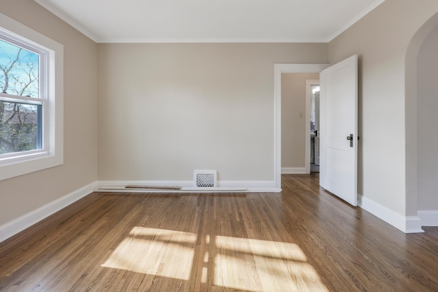 unfurnished room with arched walkways, wood finished floors, crown molding, and baseboards