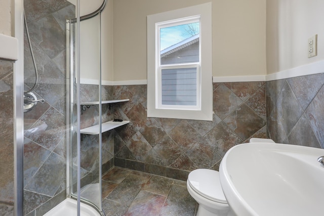 bathroom featuring tile walls, a shower stall, a sink, toilet, and stone finish floors