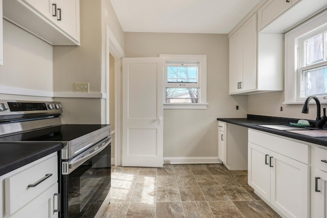 kitchen featuring stainless steel electric range, dark countertops, a sink, baseboards, and white cabinetry