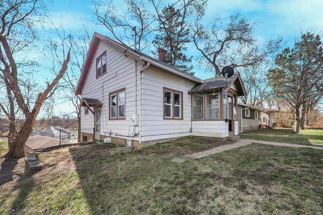 view of side of property with a chimney, a sunroom, and a lawn