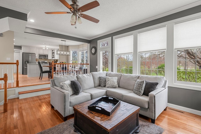 living area featuring light wood-style floors, a wealth of natural light, a ceiling fan, and visible vents