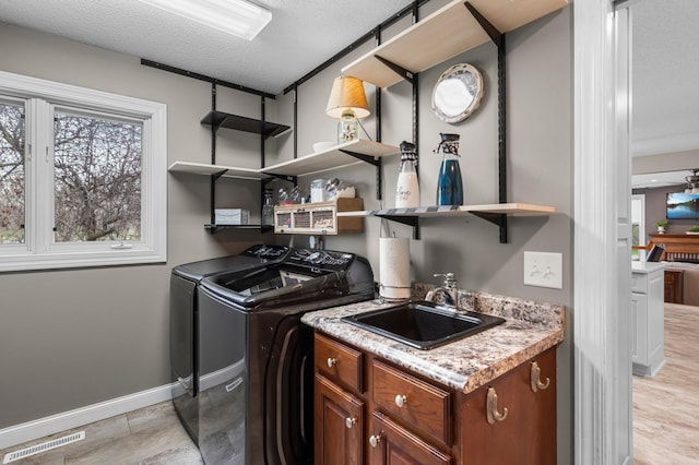 clothes washing area featuring washing machine and clothes dryer, a sink, baseboards, a wealth of natural light, and visible vents