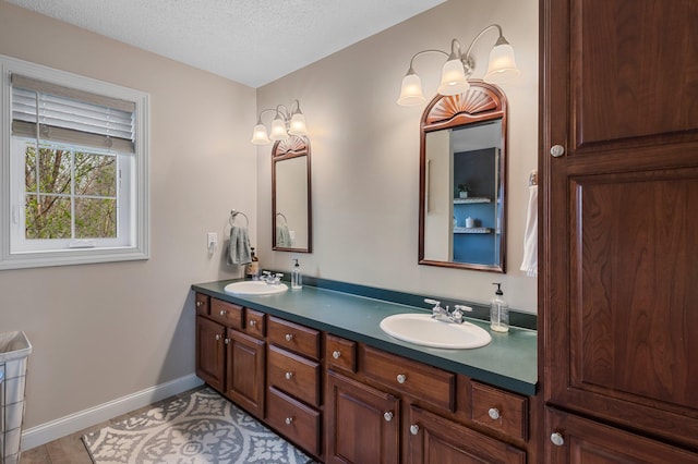 full bath featuring double vanity, a sink, a textured ceiling, and baseboards