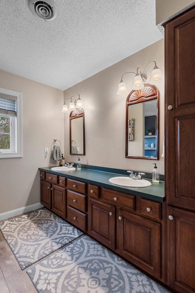 bathroom featuring double vanity, a sink, a textured ceiling, and visible vents