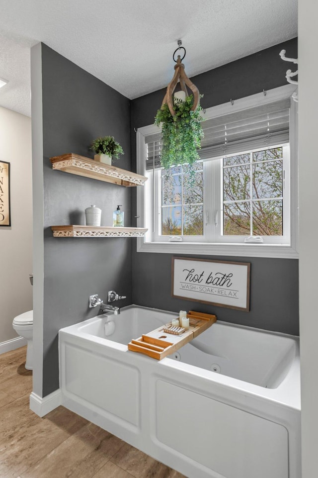 full bathroom featuring wood finished floors, toilet, a jetted tub, baseboards, and a textured ceiling