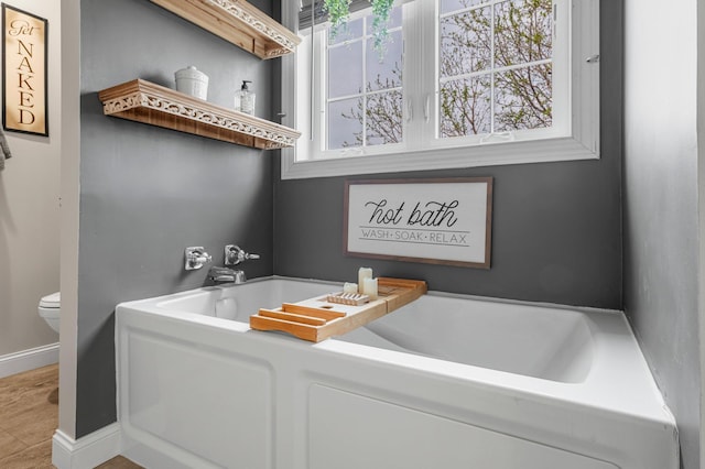 bathroom featuring baseboards, a garden tub, and toilet