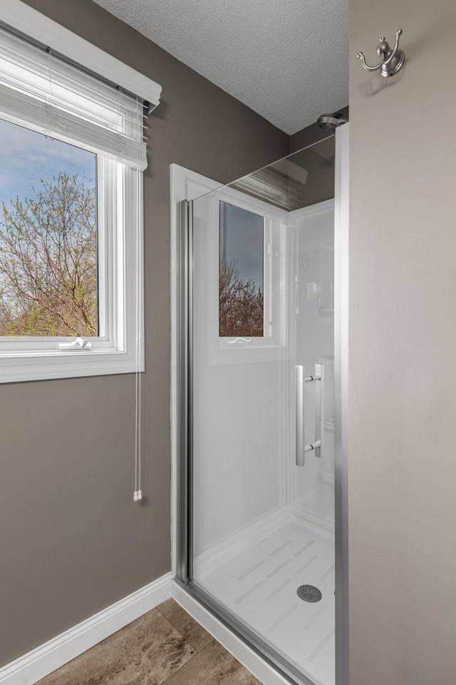 bathroom with baseboards, a stall shower, and a textured ceiling