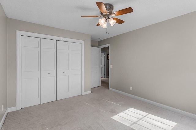 unfurnished bedroom featuring a ceiling fan, baseboards, light colored carpet, and a closet