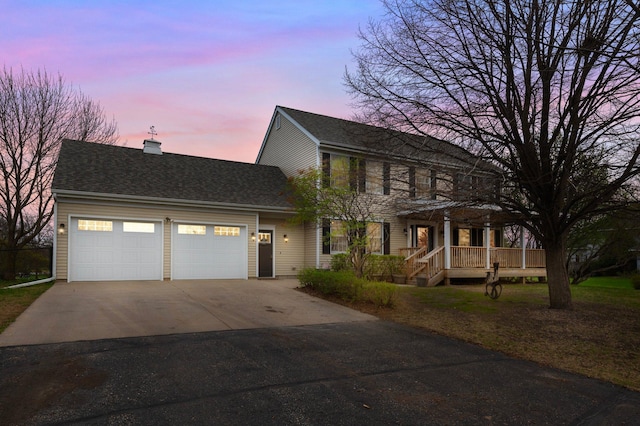 colonial house with a garage, a porch, a chimney, and driveway