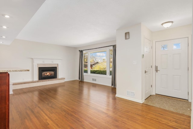 unfurnished living room featuring baseboards, visible vents, a glass covered fireplace, and wood finished floors