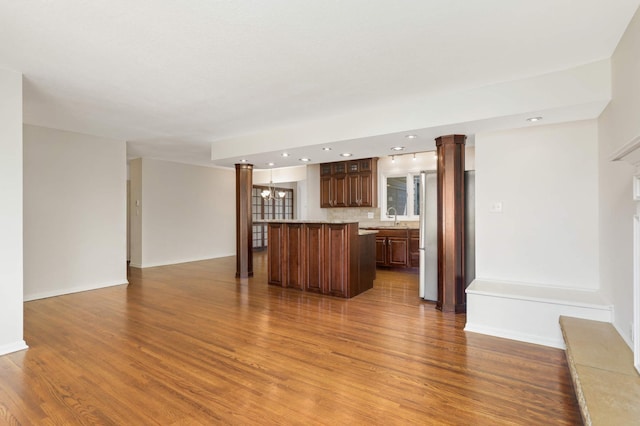 unfurnished living room featuring a sink, recessed lighting, baseboards, wood finished floors, and ornate columns