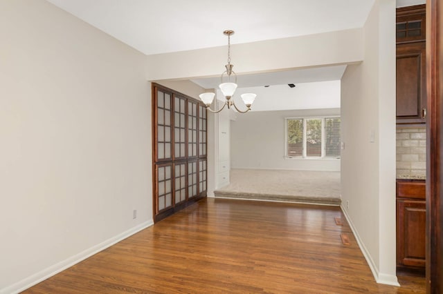 unfurnished dining area with dark wood-style flooring, baseboards, and a notable chandelier