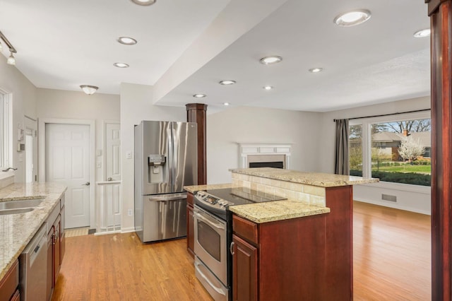 kitchen featuring reddish brown cabinets, light wood finished floors, appliances with stainless steel finishes, and a kitchen island