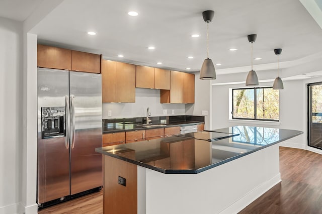 kitchen with wood finished floors, a kitchen island, baseboards, stainless steel fridge, and a sink
