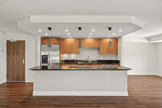 kitchen with dark countertops, stainless steel fridge, a sink, dark wood finished floors, and baseboards