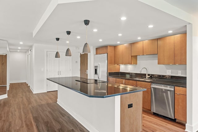 kitchen featuring dark countertops, a sink, stainless steel appliances, wood finished floors, and a kitchen island