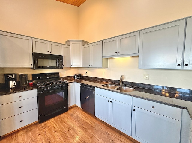 kitchen featuring black appliances, a sink, high vaulted ceiling, light wood-style flooring, and dark stone countertops