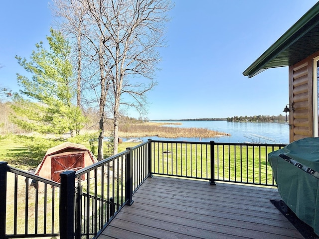 wooden terrace featuring a water view, a storage unit, an outdoor structure, a lawn, and grilling area