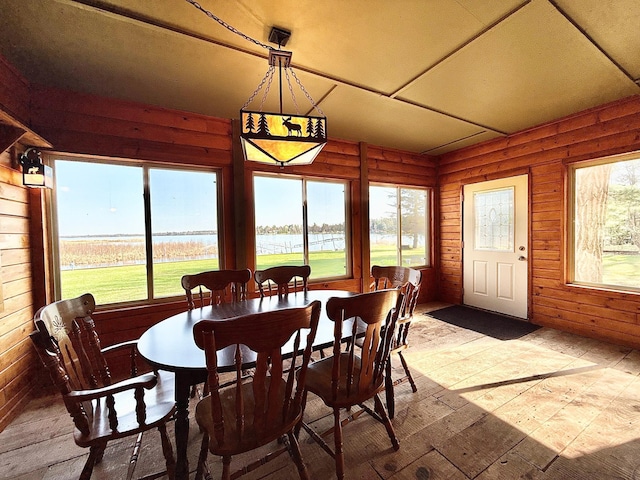 dining room featuring wood-type flooring, plenty of natural light, a water view, and wood walls