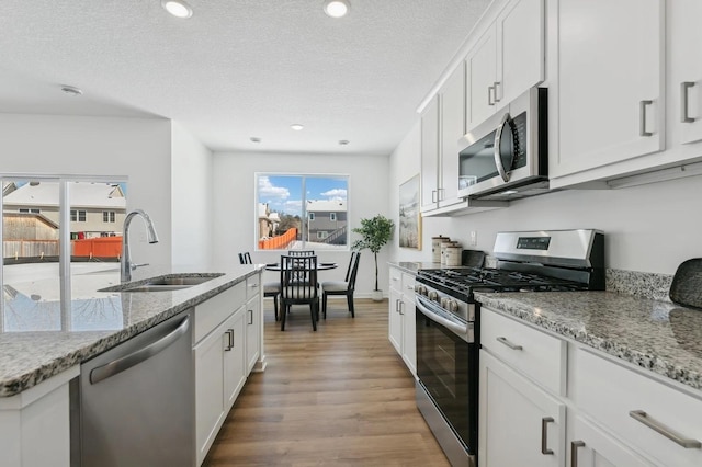 kitchen with light wood-type flooring, a textured ceiling, light stone counters, a sink, and appliances with stainless steel finishes