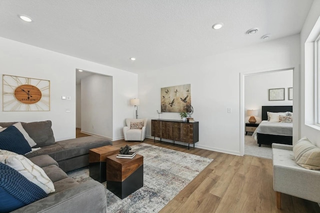 living room featuring baseboards, a textured ceiling, recessed lighting, and light wood-style flooring