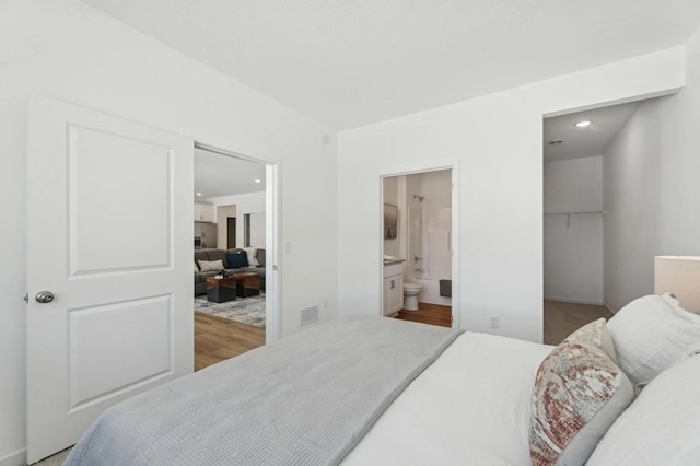 bedroom featuring stainless steel fridge with ice dispenser, ensuite bath, wood finished floors, a spacious closet, and visible vents