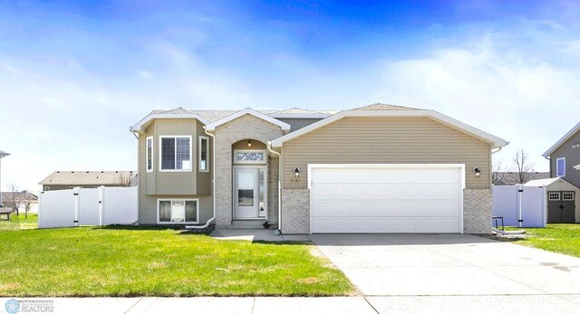 split level home featuring brick siding, a garage, concrete driveway, and a gate