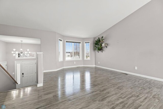unfurnished living room with a chandelier, baseboards, and wood finished floors