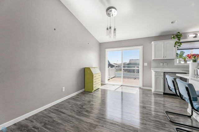 unfurnished dining area with lofted ceiling, dark wood finished floors, and baseboards