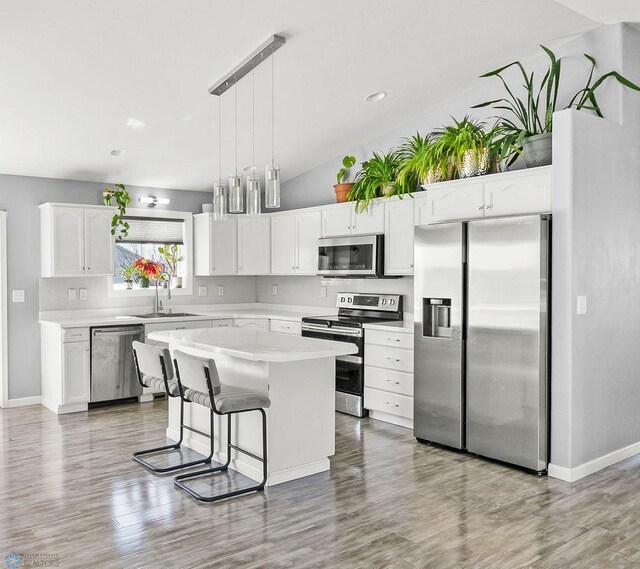 kitchen with stainless steel appliances, vaulted ceiling, a sink, white cabinets, and light countertops