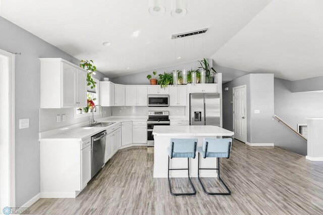 kitchen with stainless steel appliances, a sink, vaulted ceiling, light wood finished floors, and light countertops