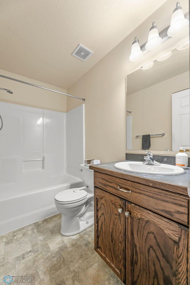 full bath with toilet, vanity, bathtub / shower combination, stone finish floors, and a textured ceiling