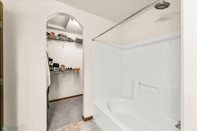 bathroom with a textured ceiling, a spacious closet, shower / bath combination, and baseboards