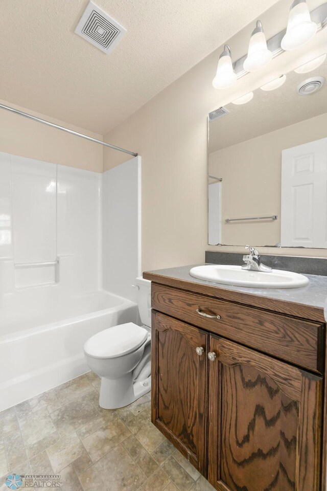 full bathroom with toilet, vanity, shower / washtub combination, stone finish flooring, and a textured ceiling