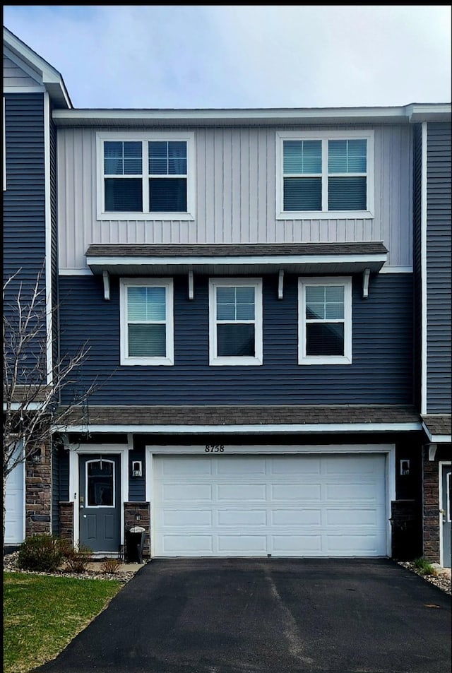 view of front facade with a garage, board and batten siding, stone siding, and aphalt driveway