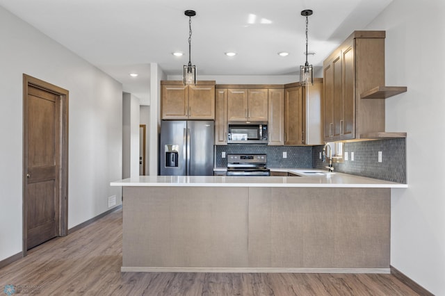 kitchen with appliances with stainless steel finishes, a sink, baseboards, light countertops, and light wood finished floors