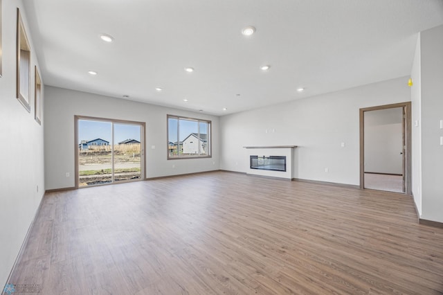unfurnished living room with light wood-style floors, recessed lighting, baseboards, and a glass covered fireplace