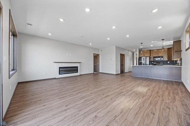 unfurnished living room featuring recessed lighting, light wood-style floors, baseboards, a glass covered fireplace, and a sink