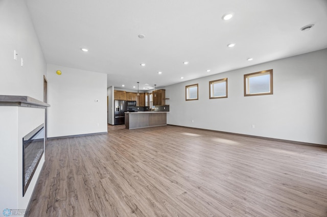 unfurnished living room featuring recessed lighting, light wood finished floors, baseboards, and a glass covered fireplace